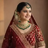 Smiling Indian bride in red bridal lehenga with green jewelry and elegant wedding makeup